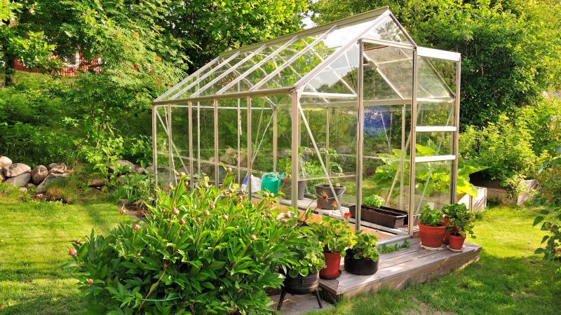 Växthus i glas med krukor och grönska runt om.