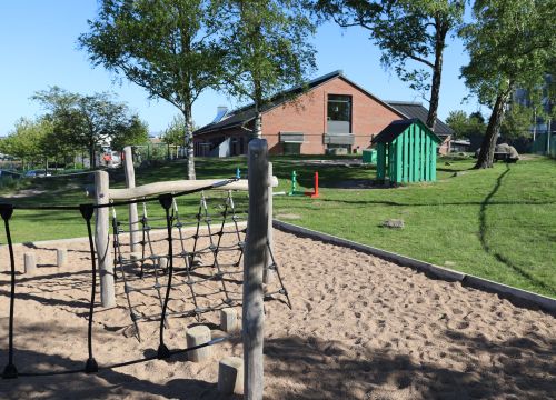 Balansbana i sand - gräsmatta med grön lekstuga i bakgrunden