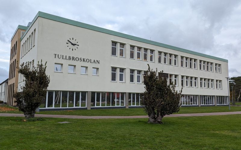 Vitbetongbyggnad med texten Tullbroskolan och en stor klocka.