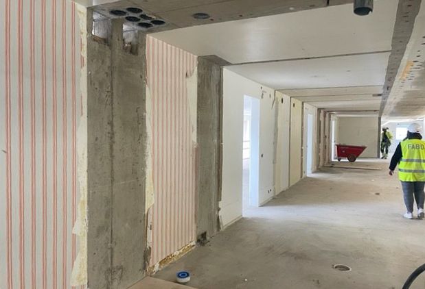 Ett stort rum med betonggolv och betongväggar. På några ställen sitter en gammal tapet med vit botten och röda ränder..