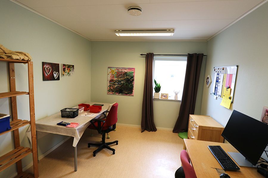 Arbetsrum med två skrivbord och hylla. På ett av skrivborden står en dator.